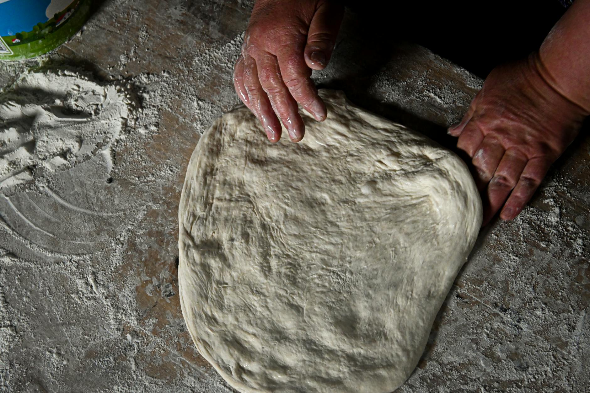 Dłonie zagniatające ciasto chlebowe na oprószonym mąką blacie